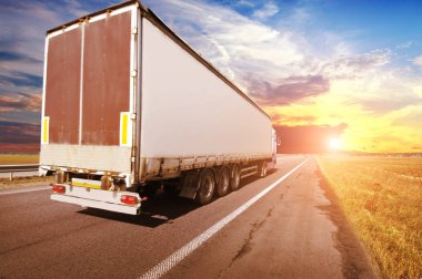 Big truck and trailer with space for text on the countryside road against sky with sunset