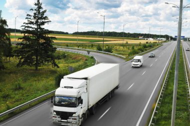 Big truck and white trailer with space for text and other cars driving fast on the countryside road against cloudy sky