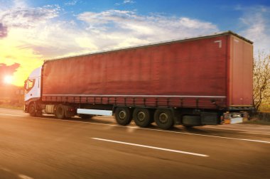 Big white truck and red trailer driving fast on countryside road with trees against sky with sunset