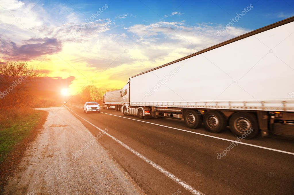 Big truck and white trailer with space for text and other vehicles on the countryside road against sky and sunset