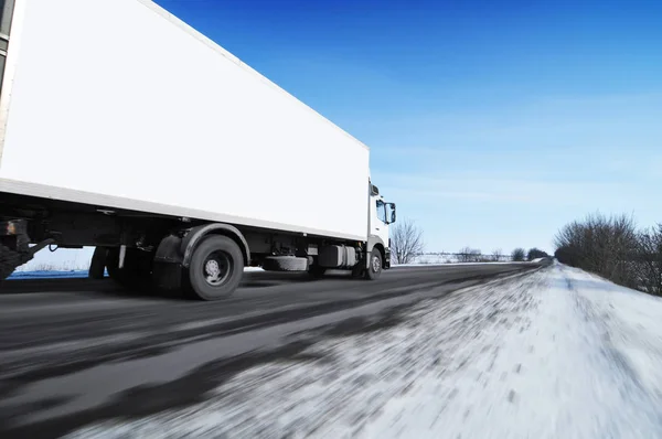 White box truck with space for text driving fast on the countryside winter road with snow against blue sky
