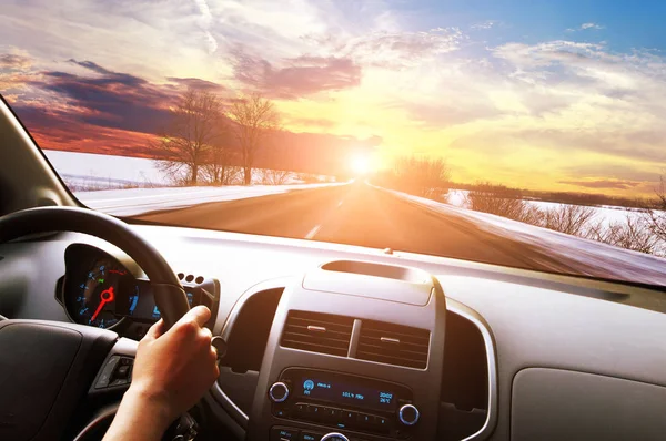 汽车仪表盘 司机手握黑色方向盘 在冬季沥青路面上行驶 蓝天夕阳西下 — 图库照片