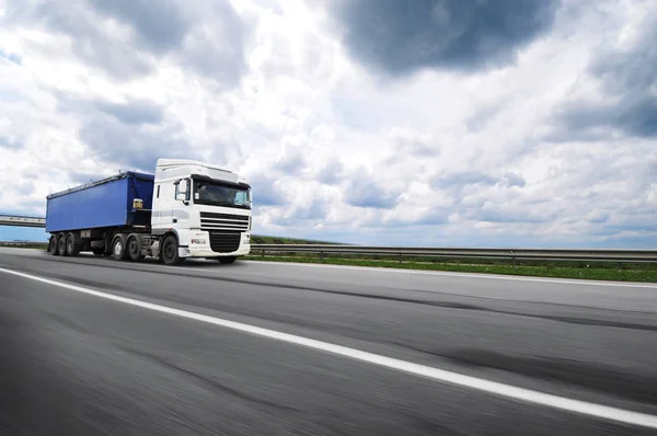 曇りの空に対する田舎道上の動きで青いトレーラー付きの大きな白いトラック — ストック写真