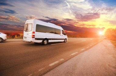 Beyaz minibüs ve diğer arabalar asfalt yolda gün batımına karşı.