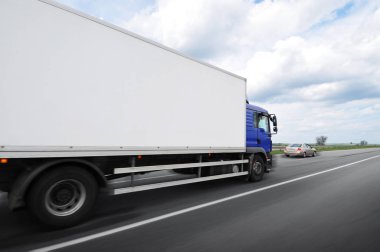 Mesajlaşmak için yeri olan büyük bir kamyon ve bulutlu gökyüzüne karşı kırsal yolda hızla giden aile arabası.