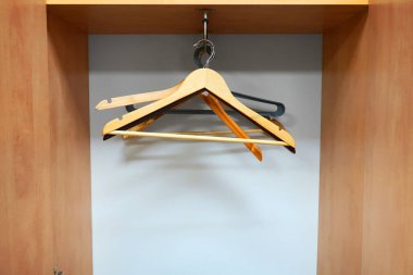 Boş ahşap dolapta farklı askılar asılı.