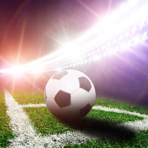 Football stadium with black and white ball on corner of field with green grass and bright lights with flashes