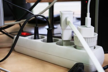 Masadaki beyaz elektrik çubuğuna takılı bir sürü fiş var.