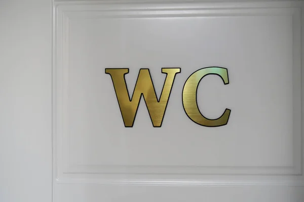 Close-up of white door with golden WC sign