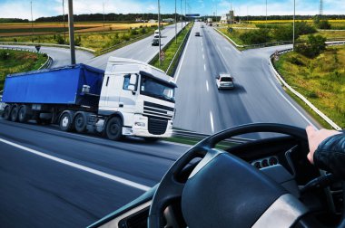 Karavanlı bir kamyon, direksiyonlu bir kamyon, arabalı bir yol ve mavi gökyüzü.