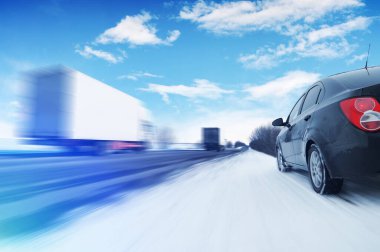 Soyut arkaplan, hareket halindeki iki beyaz kamyonet ve kırsal bir kış yolunda hareket halindeki siyah aile arabasıyla mavi gökyüzüne karşı bulutlar ve mavi ışıklar.