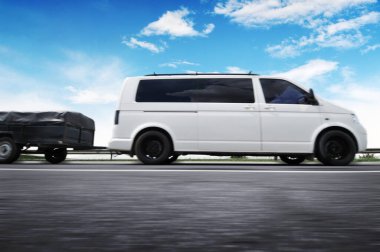 Küçük römorklu büyük beyaz minibüs mavi gökyüzüne doğru hızla ilerliyor.