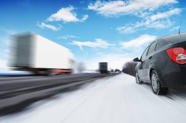 Soyut bir arka plan, hareket halindeki iki beyaz kamyonet ve kırsal bir kış yolunda hareket halindeki siyah aile arabası ile mavi gökyüzü ve bulutlara karşı hareket halinde.