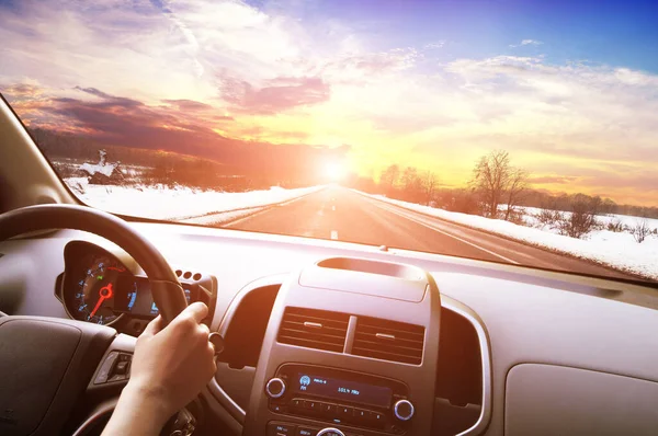 汽车仪表盘 司机手牵着黑色方向盘 与冬季沥青路面和落日的天空抗衡 — 图库照片