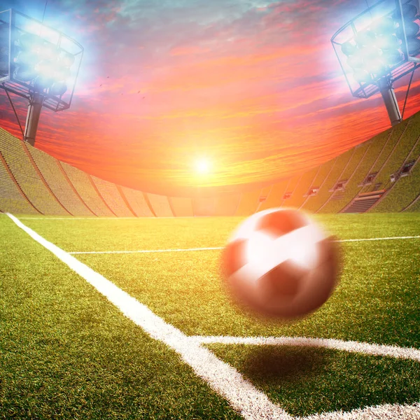 Football stadium with black and white ball in motion on corner of field with green grass and lights with flashes against sky with sunset