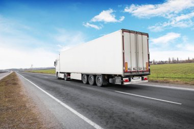 Kırsal yolda bulutlu mavi gökyüzüne karşı yazı için yeri olan büyük beyaz bir kamyon ve römork.