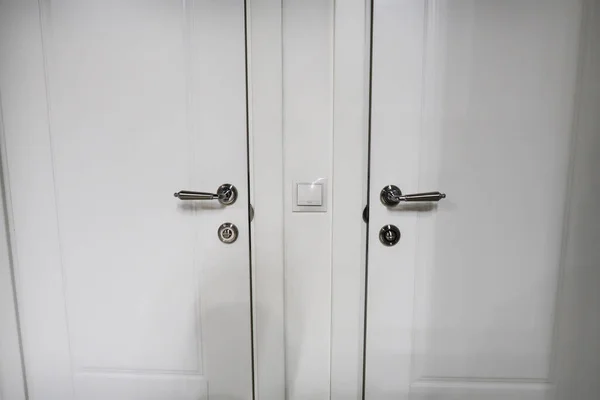 Close-up of two white doors with metallic chrome door knobs and light switch