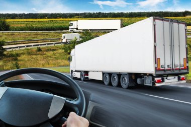 Römorklu kamyonlarla soyut arka plan, mavi gökyüzüne karşı tarlalı kamyon direksiyonu ve yol.