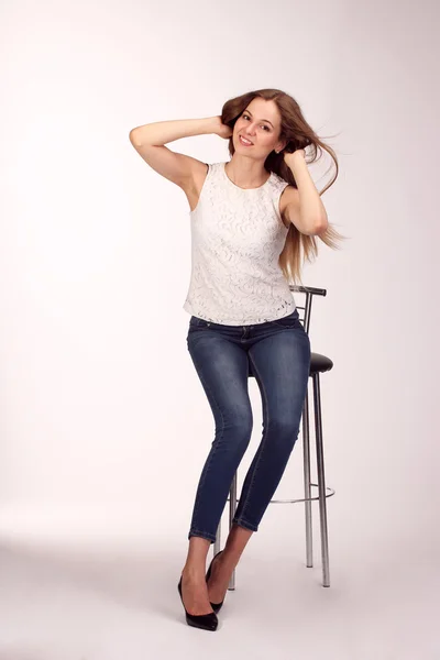 Single happy young woman sitting on a white chair in studio — Stock Photo, Image