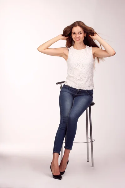 Ενιαία ευτυχισμένη νεαρή γυναίκα που κάθεται σε μια λευκή καρέκλα στο studio — Φωτογραφία Αρχείου