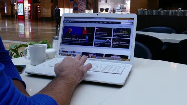 Człowiek w centrum handlowego czytanie wiadomości Bbc na laptopie — Wideo stockowe