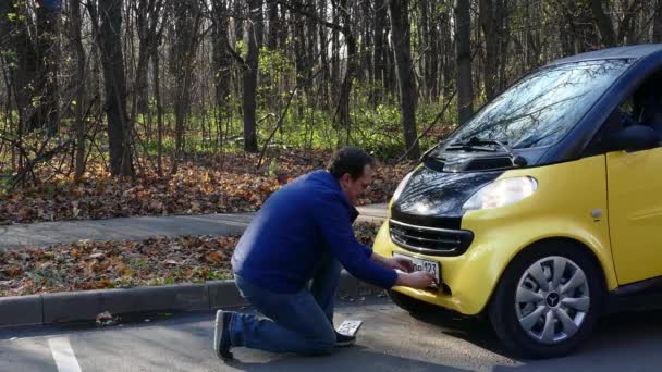 Muž předení deska s číslem vozu na malé žluté auto — Stock video