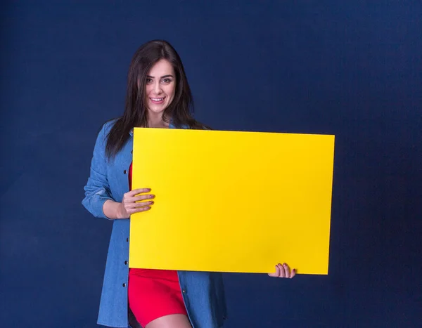 Mujer feliz sosteniendo una hoja de papel en blanco amarillo, sobre fondo azul —  Fotos de Stock