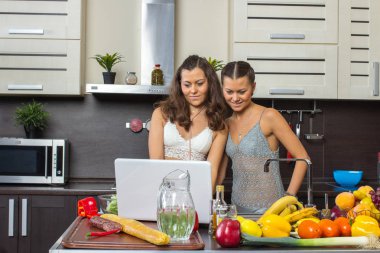 Dizüstü bilgisayar, mutfakta ayakta bakarak iki çekici kadın. 