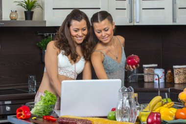 Dizüstü bilgisayar, mutfakta ayakta bakarak iki çekici kadın. 