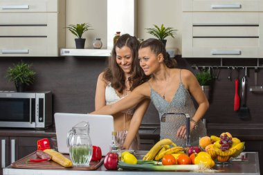 Dizüstü bilgisayar, mutfakta ayakta bakarak iki çekici kadın. 