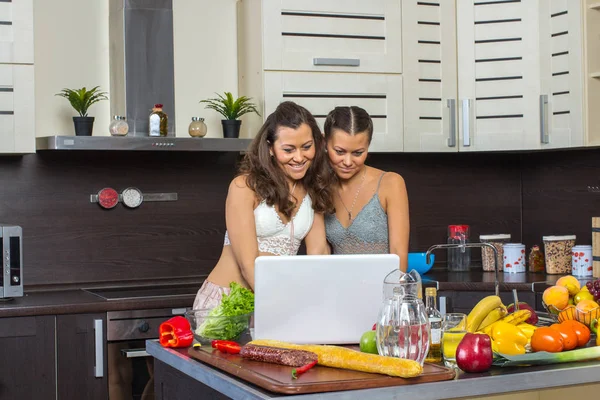 Två attraktiva kvinnor tittar på laptop, stående i köket. — Stockfoto