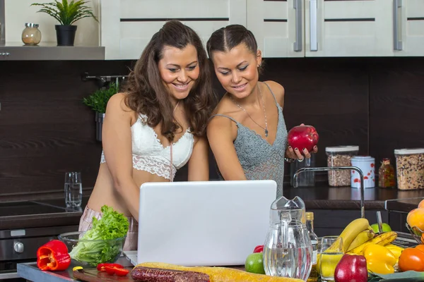 Två attraktiva kvinnor tittar på laptop, stående i köket. — Stockfoto