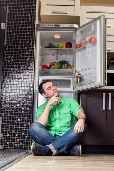 Ung Man sitter framför kylskåp — Stockfoto