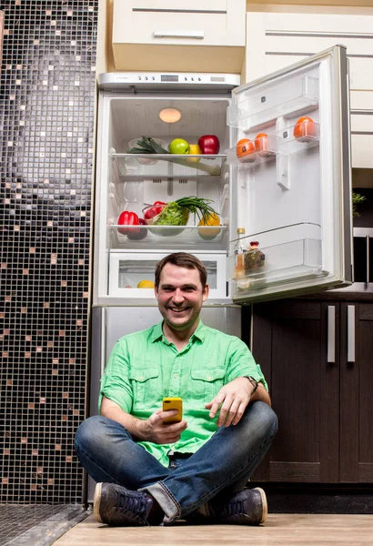 Ung Man sitter framför kylskåp — Stockfoto