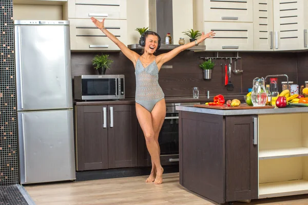 Jovem feliz dançando na cozinha com fones de ouvido . — Fotografia de Stock