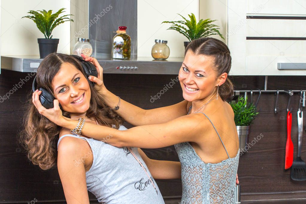 Happy young girlfriends dancing in kitchen with headphones. 