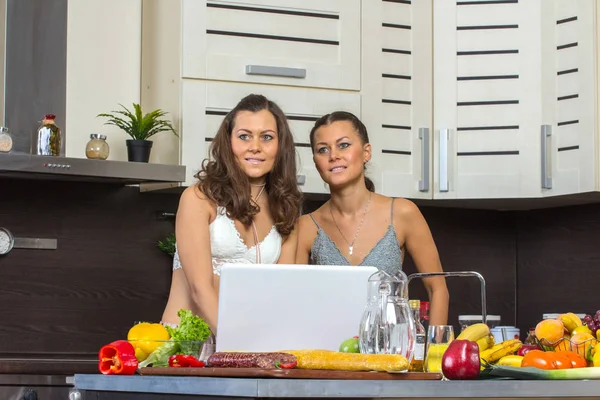 Två attraktiva tvillingar kvinnor tittar på laptop, stående i kök — Stockfoto