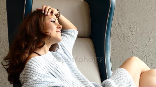 Sexy Young Pretty Woman Wearing blue Cardigan Sitting on a Chair with One Hand on her hair and Looking to windows. — Stock Video