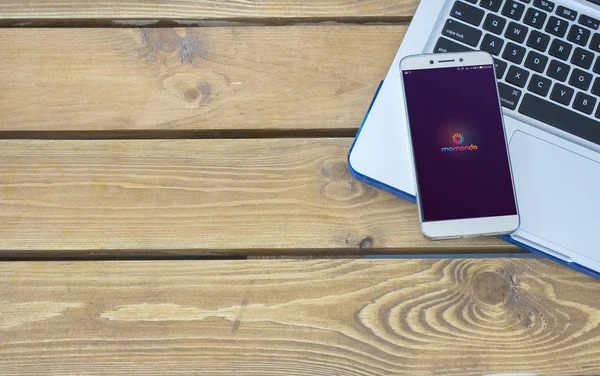 Logo Momondo sullo schermo dello smartphone posizionato sulla tastiera del laptop . — Foto Stock