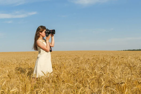 Chica bonita tomando fotos con una gran cámara negra en el campo — Foto de Stock