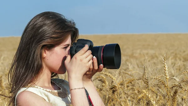 Chica bonita tomando fotos con una gran cámara negra en el campo —  Fotos de Stock
