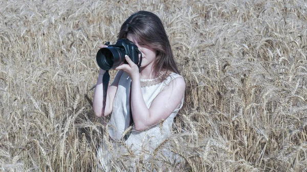 Chica bonita tomando fotos con una gran cámara negra en el campo — Foto de Stock