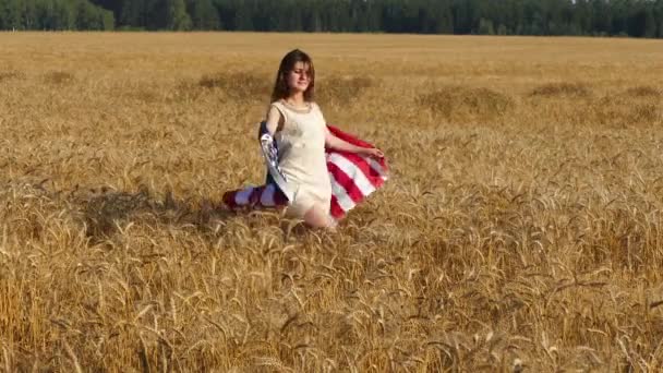 Schönheitsmädchen läuft auf gelbem Weizenfeld mit uns Nationalflagge. — Stockvideo