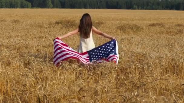 Schönheitsmädchen läuft auf gelbem Weizenfeld mit uns Nationalflagge. — Stockvideo