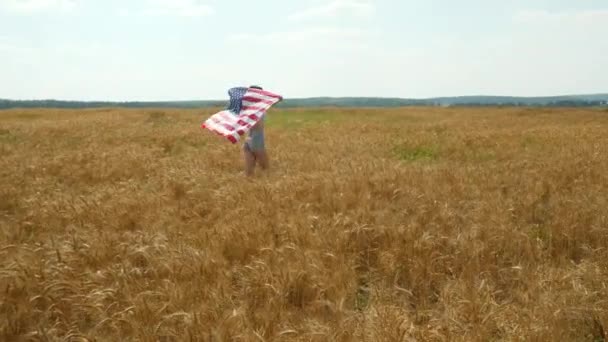 Piękna dziewczyna uruchomiona na żółte pole pszenicy z nami flagi narodowej. Szczęśliwa kobieta na zewnątrz. Żniwa — Wideo stockowe