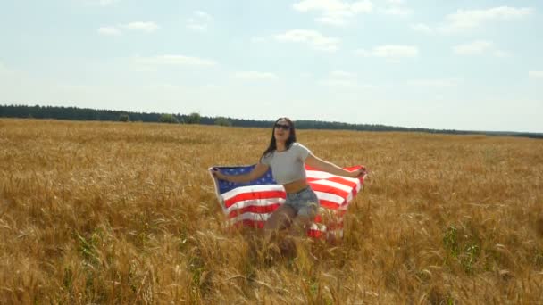 Beauty Girl Corriendo en el campo de trigo amarillo con bandera nacional de los Estados Unidos. Mujer feliz al aire libre. Cosecha — Vídeos de Stock