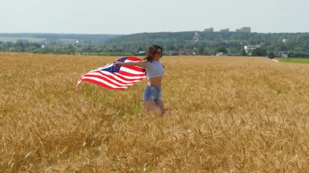 Beauty Girl Corriendo en el campo de trigo amarillo con bandera nacional de los Estados Unidos. Mujer feliz al aire libre. Cosecha — Vídeos de Stock