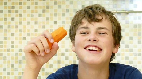 Mladý chlapec jíst mrkev s radostí. — Stock fotografie