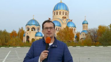 Gazeteci Ortodoks Kilisesi önünde mikrofon ile.