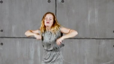 Duvarının yakınında gri giysili genç sarışın bir kadın gerçekleştirir